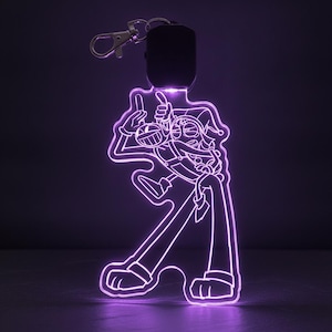 Puede incluir: Un llavero de acrílico con luz que muestra un personaje de dibujos animados con un gorro de bufón y extremidades largas, iluminado por una luz LED de color púrpura brillante. El diseño está grabado en una pieza de acrílico transparente.
