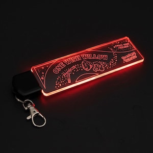 May include: A red, illuminated keychain with the words "ONE WISH WILLOW" and illustrations. It has a silver clasp and a black remote. The text "AMAZE YOUR FRIENDS!" and "You only get ONE WISH!" are also visible on the keychain.