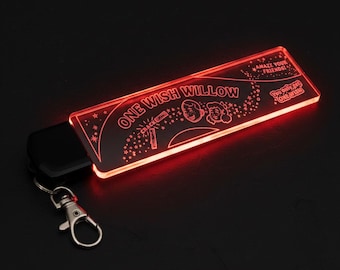 May include: A red, illuminated keychain with the words "ONE WISH WILLOW" and illustrations. It has a silver clasp and a black remote. The text "AMAZE YOUR FRIENDS!" and "You only get ONE WISH!" are also visible on the keychain.