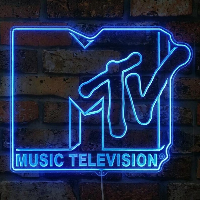 May include: A bright blue neon sign displaying the MTV logo with the text MUSIC TELEVISION underneath. The sign features a bold, outlined M and a stylized V, glowing with a vibrant blue light against a dark, textured brick wall background.