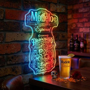 May include: A neon sign with the Modelo logo and "Especial" text, celebrating Dia de los Muertos. A glass of beer with a lime wedge, a skull figurine, and a rose are on a wooden table. The sign is mounted on a brick wall.