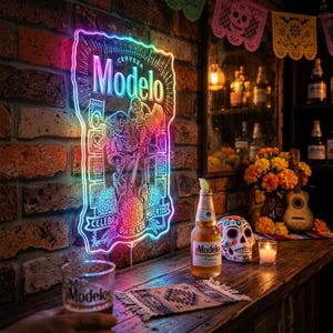 May include: A neon sign with the Modelo beer logo, featuring a colorful design with skeletons, hangs on a brick wall. A bottle of Modelo beer, a glass of beer, and a decorated skull are on a wooden bar.