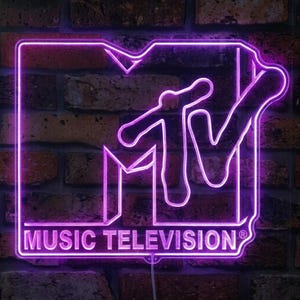 May include: A bright purple neon sign displaying the MTV logo with the text MUSIC TELEVISION and a registered trademark symbol. The sign features a bold, stylized M shape with a TV outline and emits a vibrant glow against a dark brick wall.