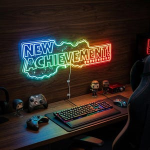 May include: A neon sign with the words "NEW ACHIEVEMENT!" in blue, green, and red. The sign is above a desk with a keyboard, mouse, and game controllers. The desk is made of wood.