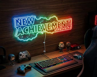May include: A colourful neon sign reading "NEW ACHIEVEMENT!" above a gaming setup. The desk features a keyboard, mouse, and game controllers. The wooden desk is the focal point of the image.