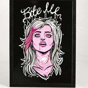 May include: Framed art print with a stylized illustration of a woman with pink skin and hair, and white accents. The artwork includes the text "Bite Me" in white script. The background is black.