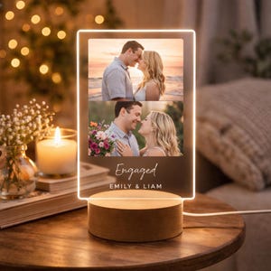 May include: A personalized LED photo frame with two engagement photos. The frame has a wooden base and displays the word "Engaged" along with the names "Emily & Liam". The photos show a couple in romantic poses.