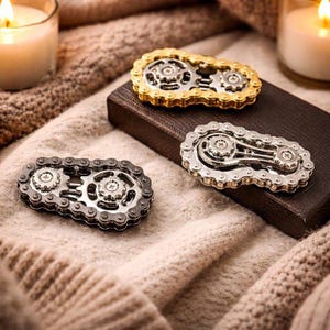 May include: Three fidget spinners constructed from metal bicycle chains and gears. One spinner is gold-toned, one is silver-toned, and one is black. Each device features two central gears connected by a chain link frame with visible screws.