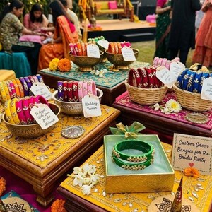 May include: A display of colorful bangles in various containers, including bowls and baskets, arranged on decorative tables. The bangles are in shades of pink, yellow, blue, and green, with some adorned with embellishments. Some tags read "Wedding Favor" and "Custom Green Bangles for the Bridal Party."