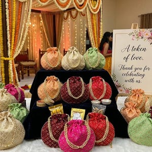 May include: A collection of beaded drawstring pouches in shades of pink, red, gold, and green. The pouches are displayed on a table with a sign that reads "A token of love. Thank you for celebrating with us."