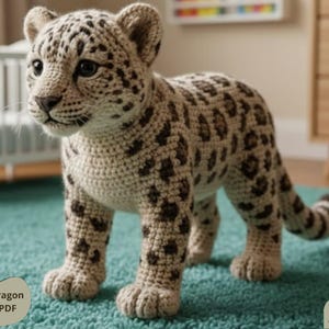 Może przedstawiać: Szydełkowany młody lampart z brązowymi i beżowymi plamami stoi na turkusowym dywanie. Ręcznie wykonane zwierzę ma szczegółowe cechy, w tym realistyczną twarz i łapy. Widoczny jest tekst "Crochet Dragon Pattern PDF" i "Digital Download".