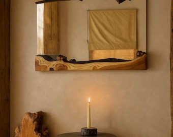 May include: A rectangular mirror with a natural wood frame, showcasing the raw edge of the wood. The mirror hangs above a small, dark metal table with a lit candle. A large piece of wood sits on the floor.