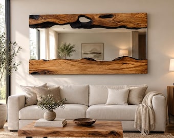 May include: A rectangular wall mirror featuring a natural live-edge wood frame with a prominent grain pattern and charred black accents along the top and bottom edges. The mirror surface reflects the interior space, including a sofa and decor.