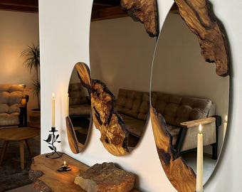 Puede incluir: Tres espejos ovalados con marcos de madera natural de borde vivo montados en una pared sobre una consola de madera a juego. Los espejos presentan bordes irregulares y la consola sostiene dos candelabros de metal negro.