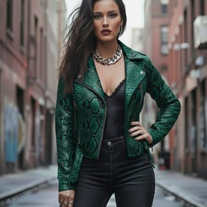 May include: A woman wearing a green snakeskin-patterned jacket, black top, and black jeans. The jacket has a classic biker style with a notched collar and zipper details. A silver chain necklace adds a touch of glamour. The background is a city street.