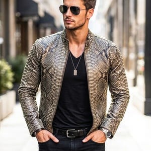 Może przedstawiać: Skórzana kurtka ze wzorem skóry węża w odcieniach szarości i brązu. Kurtka ma stójkę i zapięcie na zamek błyskawiczny. Osoba nosi czarny t-shirt, czarne dżinsy i okulary przeciwsłoneczne. Widoczny jest również srebrny naszyjnik i zegarek.