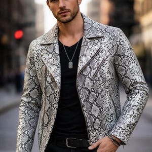 May include: A grey and white snakeskin-effect jacket. The jacket has a classic biker design with a notched collar and an asymmetrical zip. The model is wearing a black top and black jeans. The jacket's measurements are in centimeters.