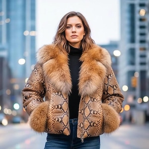 Pode incluir: Casaco castanho e bege com padrão de pele de cobra, com gola e punhos de pele. O casaco tem fecho de correr e é usado sobre uma gola alta preta. A modelo usa calças de ganga azuis.