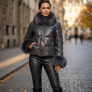 May include: A dark grey puffer jacket with a snakeskin pattern, featuring a fur collar and cuffs. The jacket is paired with black leather trousers and boots, creating a stylish winter ensemble.