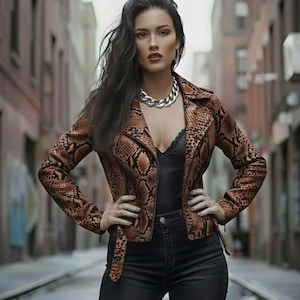Może przedstawiać: Brązowa i beżowa kurtka z wzorem skóry węża, z czarnym topem i czarnymi dżinsami. Kurtka ma kołnierz z klapami i zapięcie na zamek błyskawiczny. Srebrny naszyjnik łańcuszkowy jest noszony.