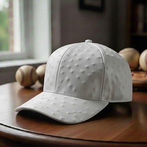 May include: A white baseball cap with a textured surface, featuring a curved brim and a button on top. The cap is displayed on a wooden table, with baseballs in the background.