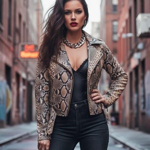 May include: A snakeskin-patterned jacket with a zipper closure. The jacket is paired with a black top, black jeans, and a silver chain necklace. The model is standing in an alleyway.