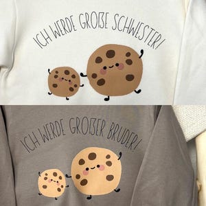 Könnte beinhalten: Zwei Sweatshirts, eines weiß und eines grau, jeweils mit einem Cartoon-Keks-Design. Das weiße Sweatshirt sagt "Ich werde große Schwester!" und das graue sagt "Ich werde großer Bruder!"