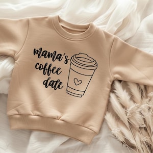 Op de afbeelding: Een beige sweatshirt met de tekst "Mama's coffee date" en een koffiekopje met een hartje. De sweatshirt is gemaakt van een zacht materiaal en is ontworpen voor kinderen.