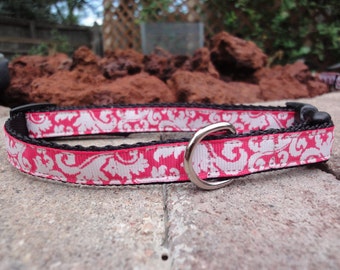 May include: A pink dog collar with a white damask pattern and a silver metal buckle.