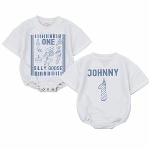May include: Two white short-sleeved baby bodysuits. The left one features a blue graphic with a goose, balloons, a cake, and the text "ONE SILLY GOOSE". The right one displays the name "JOHNNY" in blue letters above a blue candle shaped like a number one.