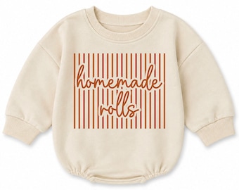 May include: A cream-colored long-sleeve romper with a ribbed crew neckline and cuffs. The center features a rectangular graphic with vertical rust-colored stripes and the text "homemade rolls" written in a cursive, rust-colored script font.