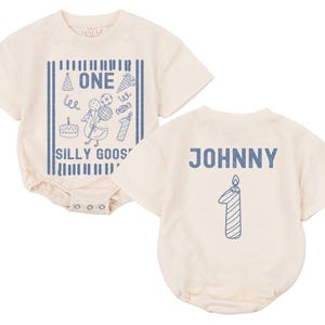 May include: A cream-colored short-sleeve bodysuit featuring a blue graphic of a goose with balloons, a cake, and the text ONE SILLY GOOSE on the front, and the name JOHNNY with a number one candle graphic on the back.