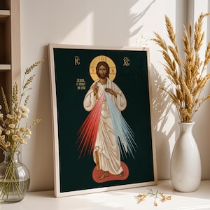 Puede incluir: Obra de arte religiosa enmarcada que representa a Jesús con un halo, vestido con túnicas blancas. La imagen incluye el texto «Jesús, confío en ti» y rayos de luz roja y azul. La obra se exhibe sobre una superficie blanca.