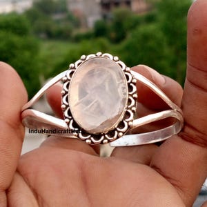 Peut inclure: Un bracelet manchette en argent orné d'une grande pierre précieuse ovale blanc translucide au centre. La pierre est sertie dans un cadre métallique décoratif festonné. Le bracelet se compose de deux fils d'argent divisés qui se rejoignent.