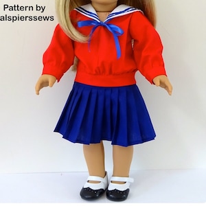 May include: A red and blue sailor outfit for a doll. The outfit includes a red long-sleeved shirt with a white sailor collar and blue ribbon, and a blue pleated skirt.