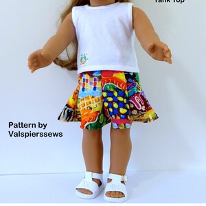 May include: A doll wearing a white sleeveless shirt and a colorful, patterned skirt. The skirt has a variety of colors and shapes, including squares, circles, and swirls. The doll is wearing white sandals.