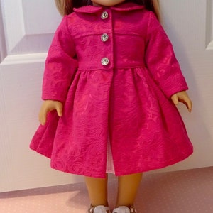 May include: A pink doll coat with a white collar and buttons. The coat has a floral pattern and is made of a soft fabric.