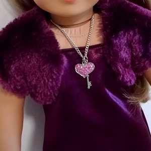 Può includere: Un bolero in pelliccia sintetica viola con un abito in raso viola abbinato e una collana d'argento a forma di cuore con una chiave e strass rosa. Il testo "Pattern by Valsgierssews" è visibile nell'angolo in basso a destra dell'immagine.
