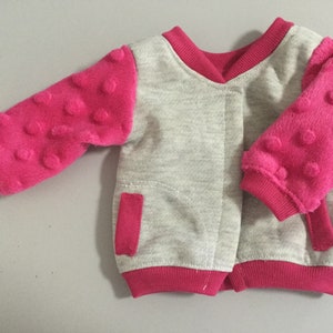May include: A gray and pink baby jacket with a zipper closure and textured pink sleeves.