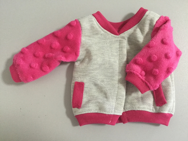 May include: A gray and pink baby jacket with a zipper closure and textured pink sleeves.