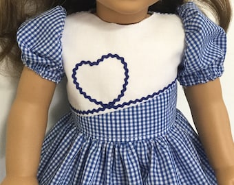 May include: A blue and white gingham dress with a white bodice and a blue heart design. The dress has puffed sleeves and a gathered skirt.