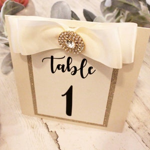 Gold Glitter Hochzeit Tischnummern mit Double Ivory Bow & Strass Juwel | Elegante Empfangskarten