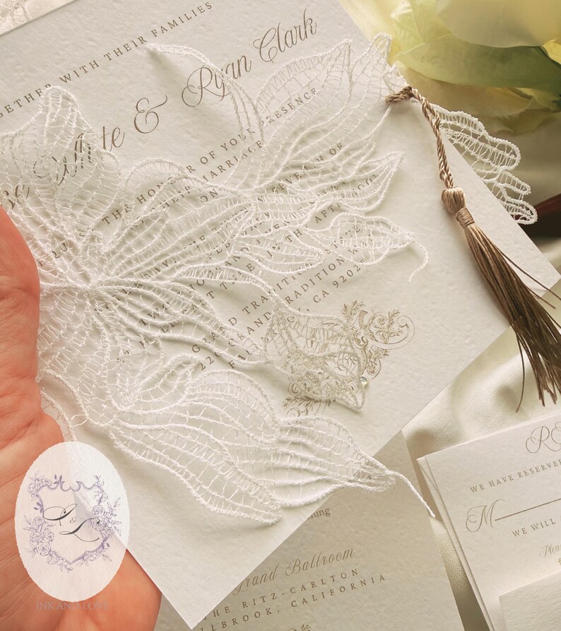 Puede incluir: Elegante invitaci&oacute;n de boda con intrincados detalles de encaje blanco. La invitaci&oacute;n presenta los nombres "Mitte & Ryan Clark" e incluye una borla decorativa. El dise&ntilde;o es cl&aacute;sico y sofisticado, perfecto para un evento formal.