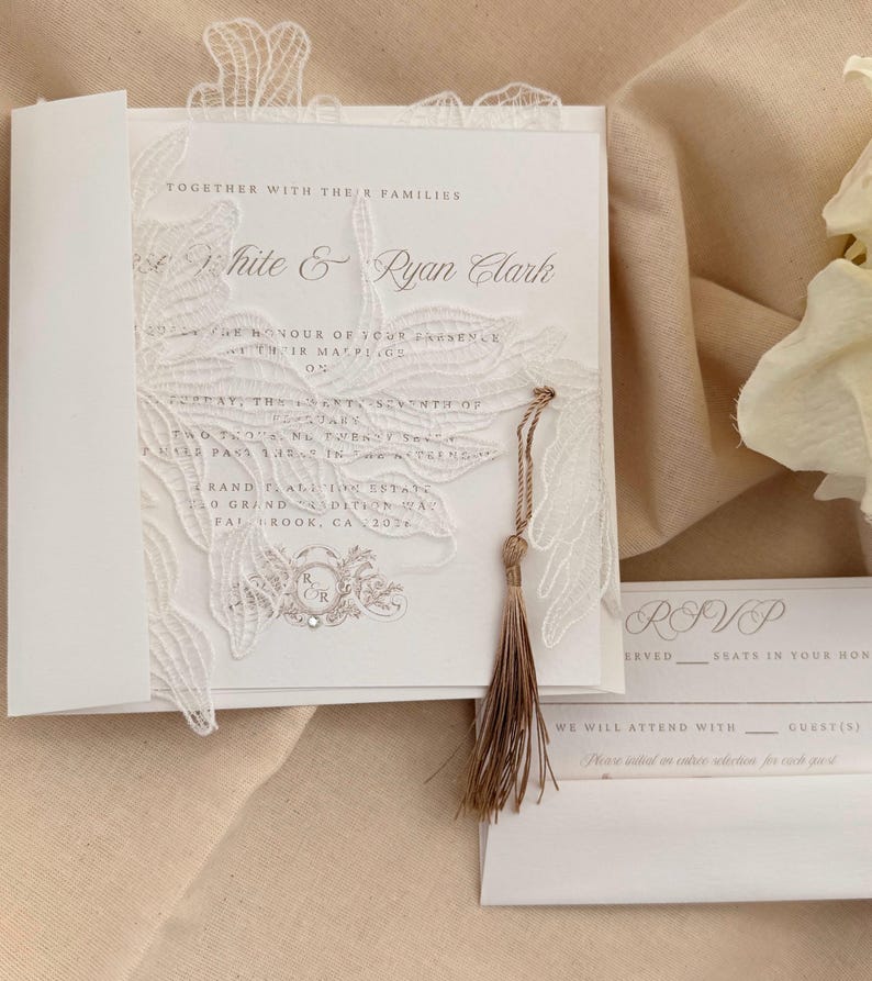 Puede incluir: Elegante invitaci&oacute;n de boda blanca con delicados detalles de encaje y una borla. La invitaci&oacute;n presenta los nombres "White & Ryan Clark" e informaci&oacute;n de RSVP. Un dise&ntilde;o sofisticado para una ocasi&oacute;n especial.