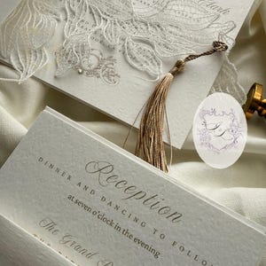 Puede incluir: Elegante juego de invitaciones de boda con un dise&ntilde;o floral cortado con l&aacute;ser y una borla. La invitaci&oacute;n incluye los nombres "Ryan Clark" y detalles de la "Recepci&oacute;n". El juego incluye un sello con iniciales y un sello de cera dorado.