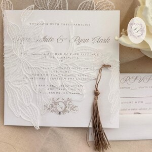 Puede incluir: Elegante invitaci&oacute;n de boda blanca con intrincados detalles de encaje floral. La invitaci&oacute;n presenta los nombres 'Rose White & Ryan Clark' e incluye una borla. Tambi&eacute;n se ve una tarjeta RSVP a juego y una pegatina con iniciales.