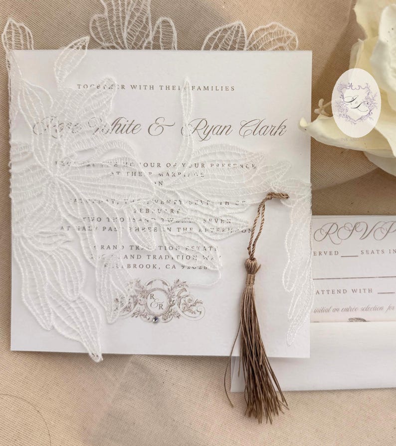 Puede incluir: Elegante invitaci&oacute;n de boda blanca con intrincados detalles de encaje floral. La invitaci&oacute;n presenta los nombres 'Rose White & Ryan Clark' e incluye una borla. Tambi&eacute;n se ve una tarjeta RSVP a juego y una pegatina con iniciales.