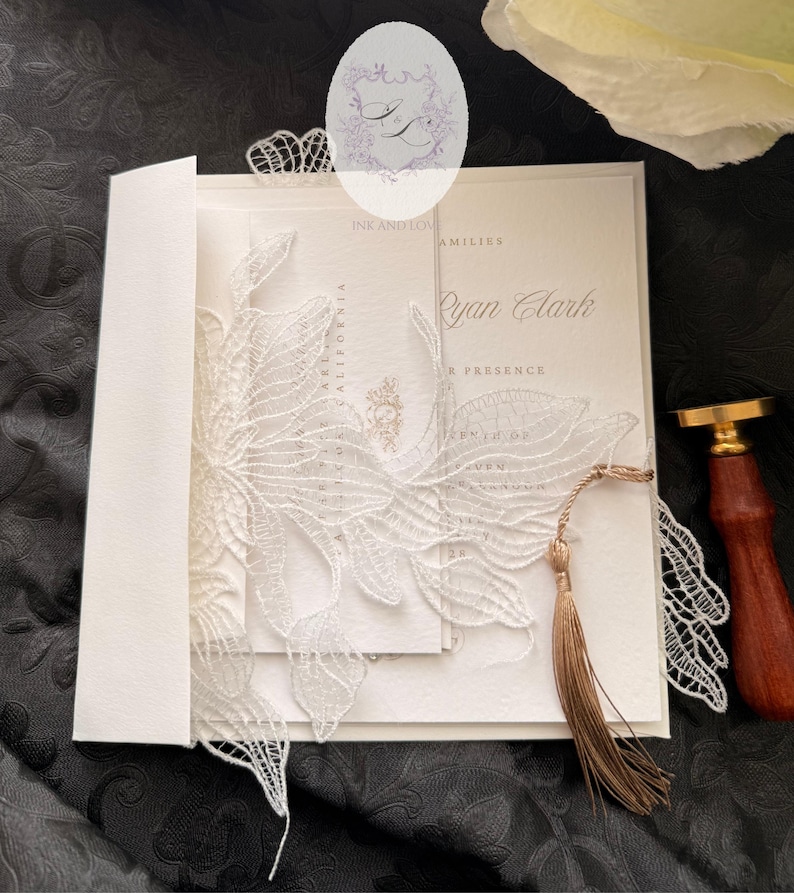 Puede incluir: Invitaci&oacute;n de boda marfil con una superposici&oacute;n de encaje blanco. La invitaci&oacute;n presenta el nombre "Ryan Clark" y est&aacute; acentuada con una borla dorada. Un sello de cera y un sobre completan el elegante dise&ntilde;o.