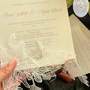Puede incluir: Invitaci&oacute;n de boda marfil con escritura elegante, con los nombres Rose White & Ryan Clark. La invitaci&oacute;n incluye un delicado adorno de encaje y una borla de madera. Se ven tarjetas de confirmaci&oacute;n de asistencia y recepci&oacute;n adicionales.