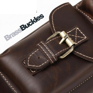 May include: Close-up of a brown leather bag with a brass buckle closure. The bag features white stitching details and the text "Brass Buckles" in the upper left corner. The leather has a textured appearance.